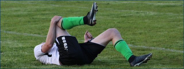 Fußballspieler liegt mit Schmerzen am Boden und hält sich das Knie